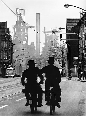 © Walter Vogel, Schornsteinfeger unterwegs auf der Kaiser-Wilhelm-Straße, im Hintergrund die August-Thyssen-Hütte, Duisburg-Bruckhausen, 1965